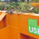 Ein orangener Container mit dem USB Logo, befüllt mit Grünschnitt