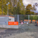 Eingezäunt stehen mehrere orangene Container, im Hintergrund sind Bäume