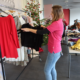 Eine Frau hängt Klamotten an eine Kleiderstange, im Hintergrund ist ein Tisch mit Kleidung.