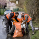 Zwei Männer mit Warnweste packen Müll am Straßenrand in einen Stadtputzsack.