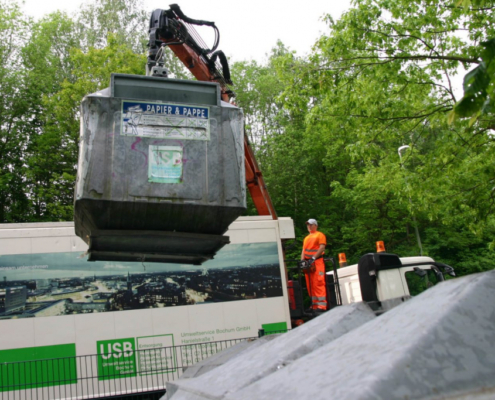 Ein Container mit der Aufschrift Papier und Pappe wird von einem LKW hochgehoben und geleert