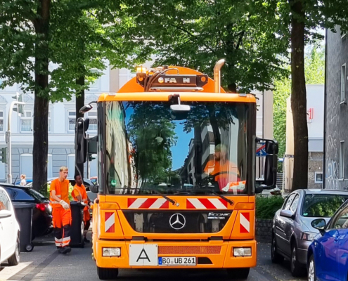 Ein Müllauto von vorne in einer schmalen Straße, am Rand sind Bäume