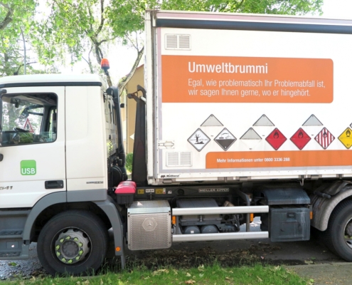 Ein weißer LKW mit der Aufschrift Umweltbrummi und mehreren Warnzeichen.