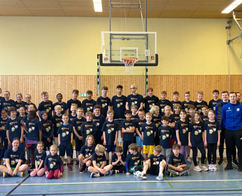 Mehrere Kinder und Betreuer stehen in einer Sporthalle unter einem Basketballkorb.