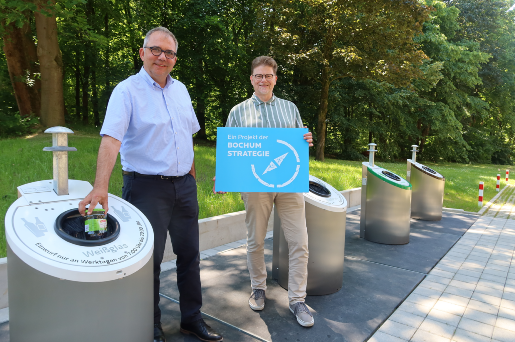 Ein Mann entsorgt Weißglas. Neben ihm steht ein weiterer Mann mit einem Schild mit Aufschrift Ein Projekt der Bochum Strategie