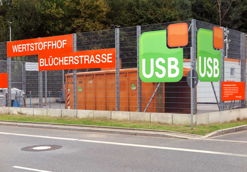 Ein Zaun mit Aufschrift Wertstoffhof Blücherstrasse und USB