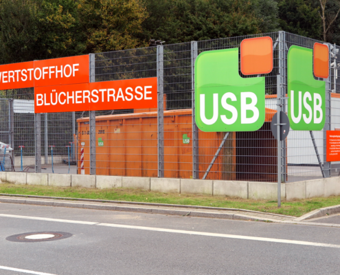 Ein Zaun mit Aufschrift Wertstoffhof Blücherstrasse und USB