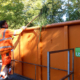 Ein Mitarbeiter wirft Grünschnitt in einen Orangenen Container mit dem USB Logo