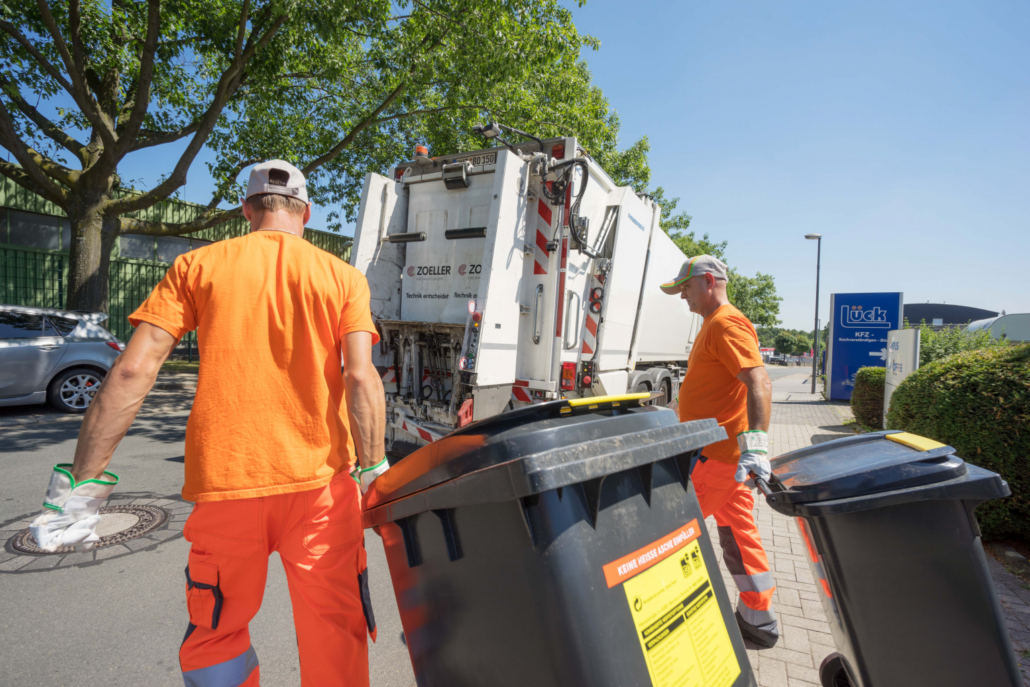 Zwei Müllmänner bringen Mülltonnen zum Müllwagen