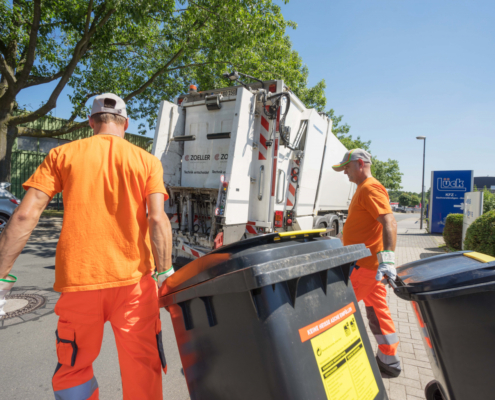 Zwei Müllmänner bringen Mülltonnen zum Müllwagen