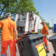 Zwei Müllmänner bringen Mülltonnen zum Müllwagen