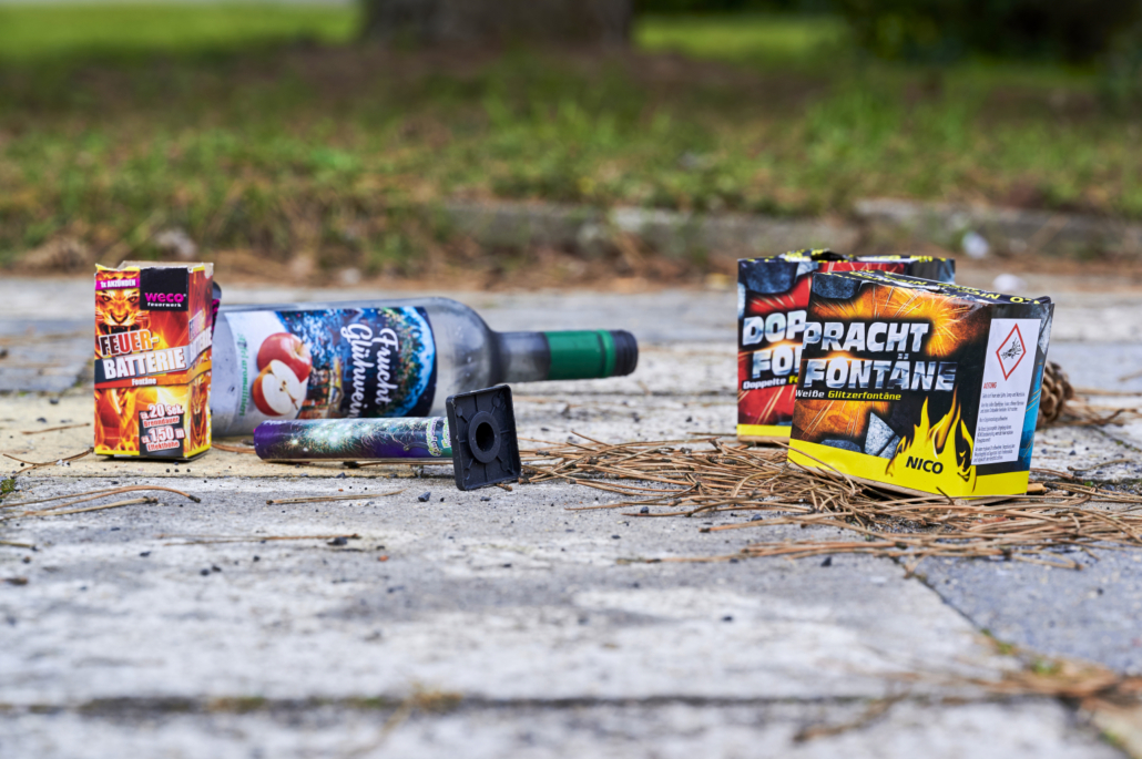 Auf Pflastersteinen liegen Feuerwerkskörper und eine Glasflasche