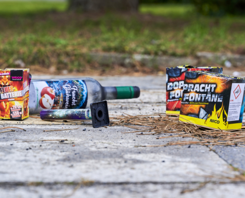 Auf Pflastersteinen liegen Feuerwerkskörper und eine Glasflasche