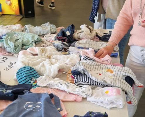 Auf einem Tisch liegen Babyklamotten zwei Frauen schauen sich die Sachen an