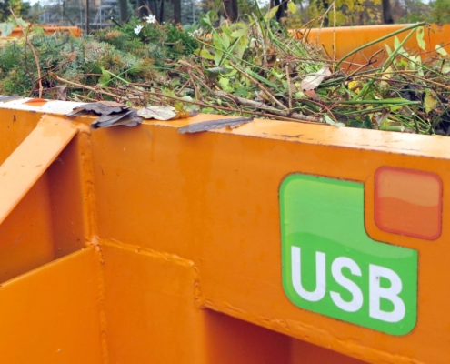 Ein orangener Container mit dem USB Logo, befüllt mit Grünschnitt