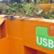 Ein orangener Container mit dem USB Logo, befüllt mit Grünschnitt
