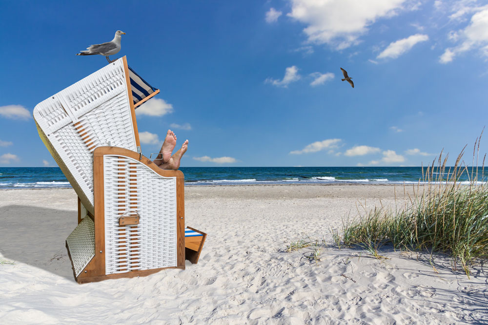 Ein Strandkorb an einem sonnigen Sandstrand mit Meer im Hintergrund
