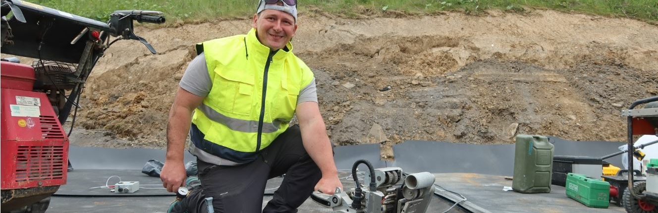 Arbeiter lächelt in Kamera und hält ein Baugerät in der Hand