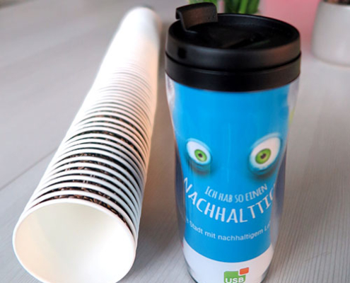 Blauer Becher mit Augen steht neben liegenden Kaffeebecher