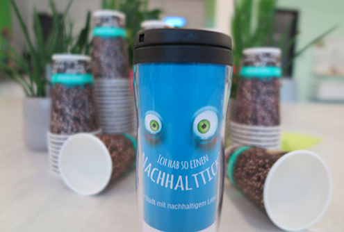 Ein Blauer Becher mit Augen. Im Hintergrund sind Coffe-to-go-Becher