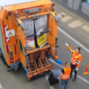 Zwei Frauen in orangenen Westen laden Müll in einen Müllwagen