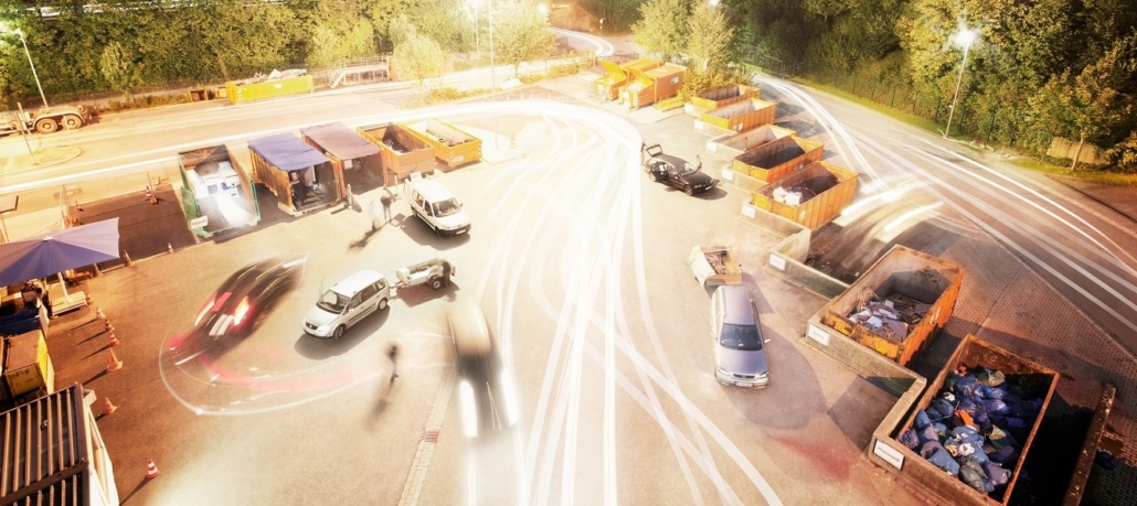 Auf einer Asphaltfläche stehen mehrere Fahrzeuge und am Rand mehrere orangene Container