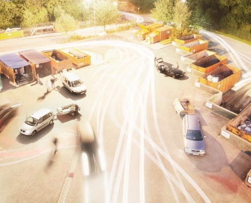 Auf einer Asphaltfläche stehen mehrere Fahrzeuge und am Rand mehrere orangene Container